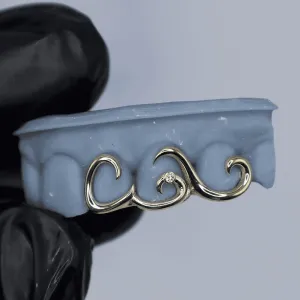 Custom white gold 3-tooth bottom grillz with abstract wavy scrollwork design and a single bezel-set diamond at center, shown on a dental cast